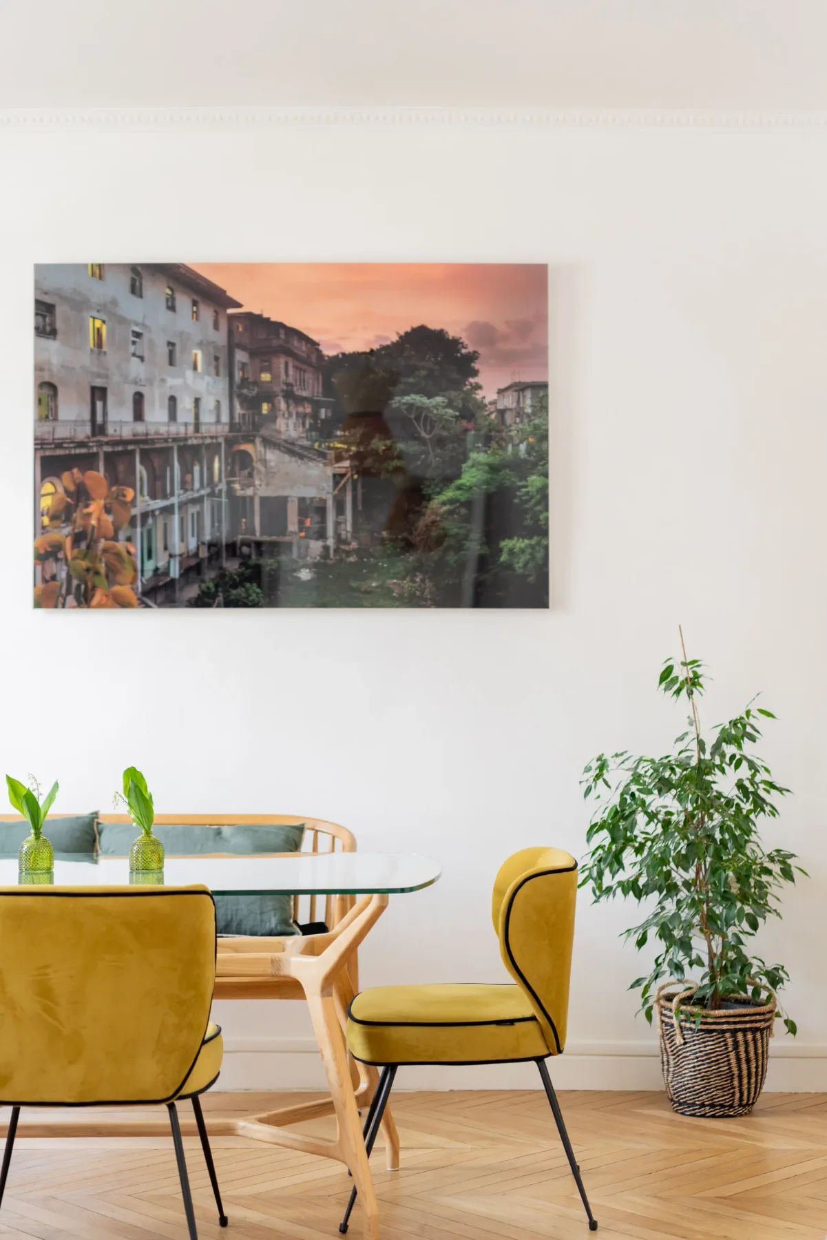 Un comedor con asientos amarillos, una mesa de vidrio y una vista urbana enmarcada.