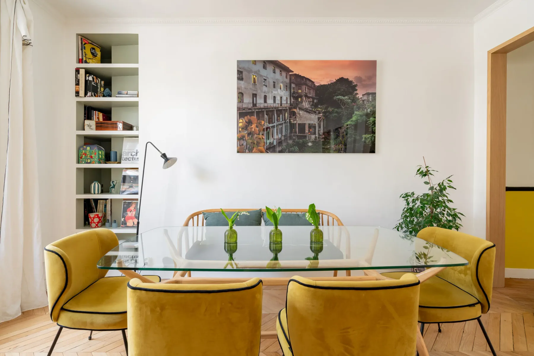 Comedor con una mesa de vidrio, asientos amarillos y un cuadro en la pared.