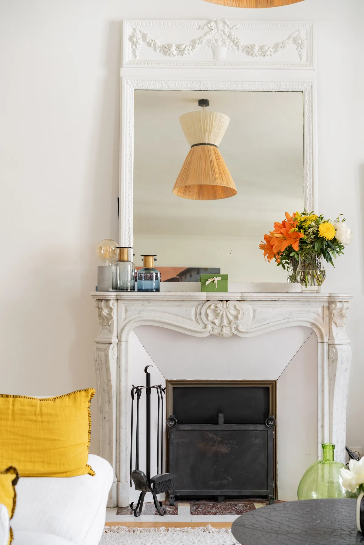 Una sala de estar con una chimenea ornamentada, un espejo grande y un cojín amarillo.