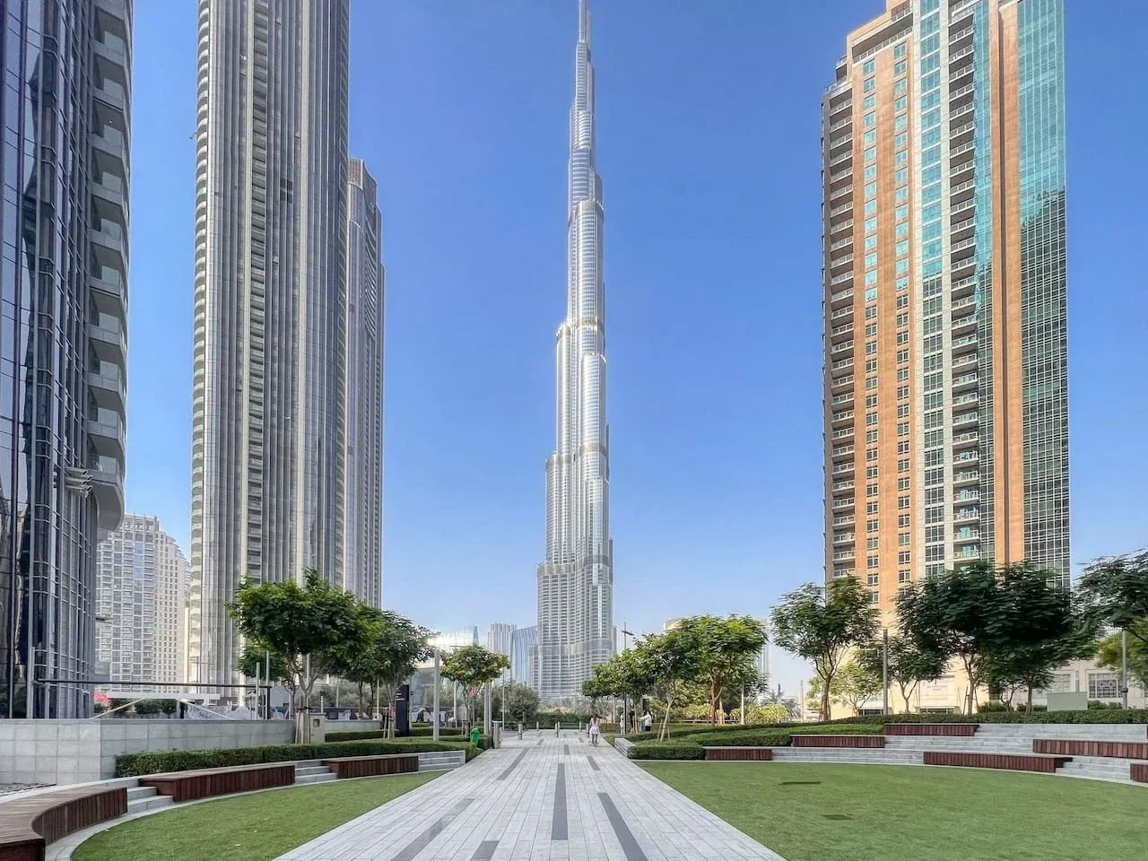 A landscaped urban plaza with paved walkways and tall surrounding buildings.
