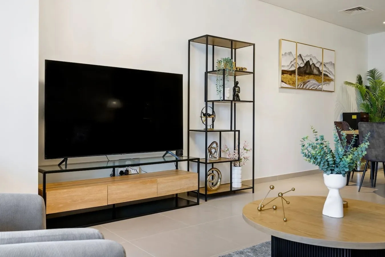 A living room with a large television, shelving, and a round coffee table.