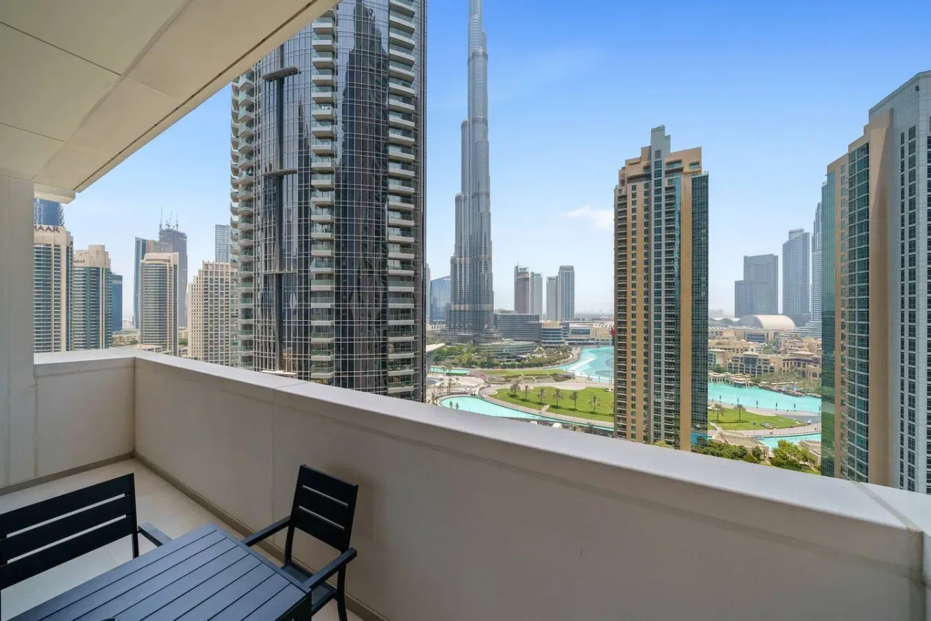 A balcony seating area overlooks a cluster of high-rise buildings and landscaped grounds.