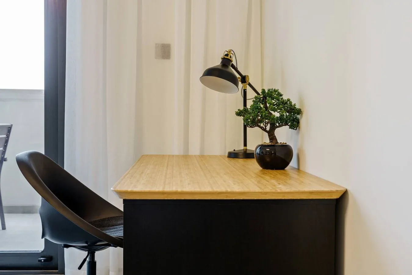 A desk with a lamp and potted plant stands beside a chair.