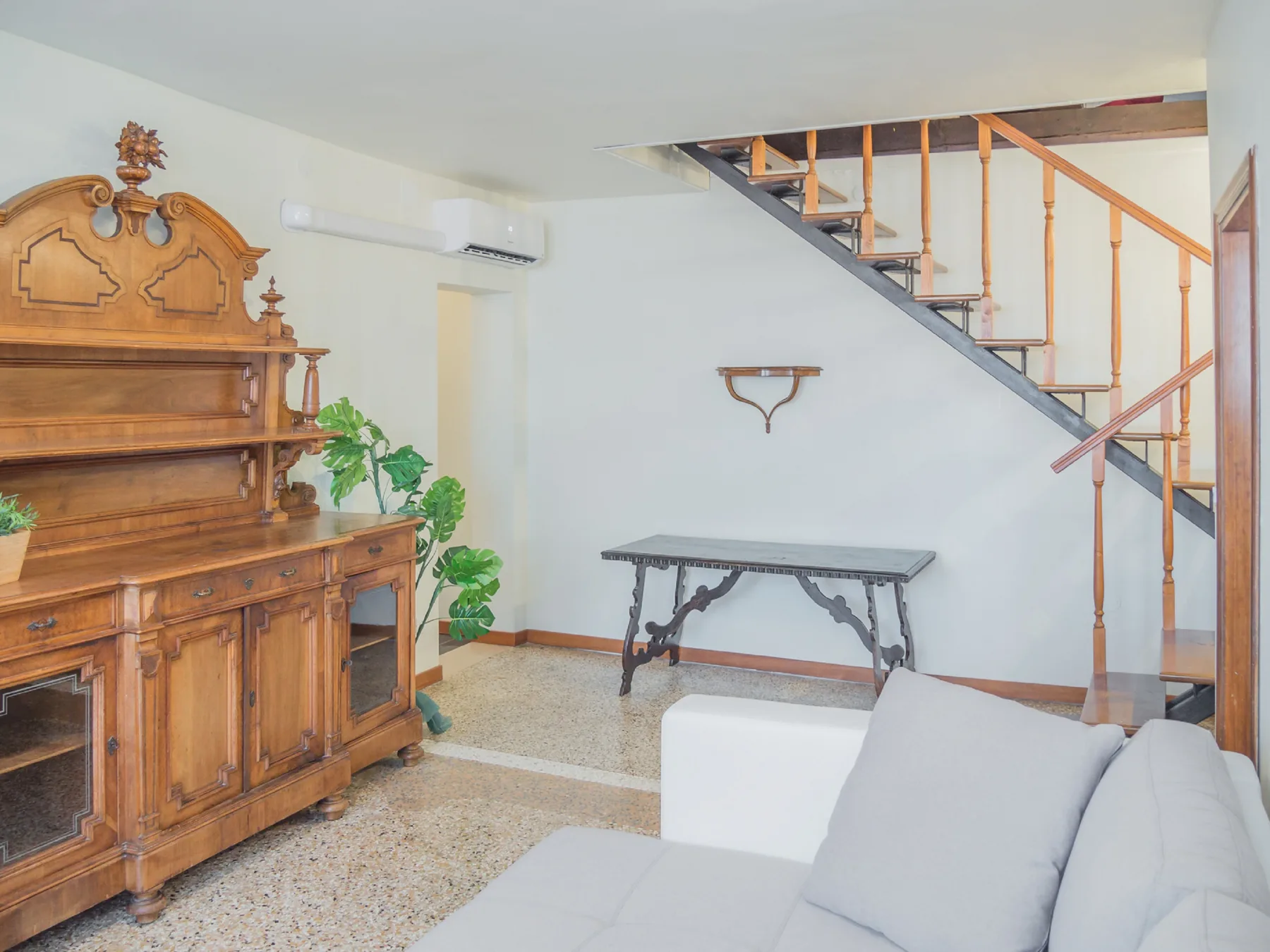A living room with a wooden cabinet, a table, and a staircase.