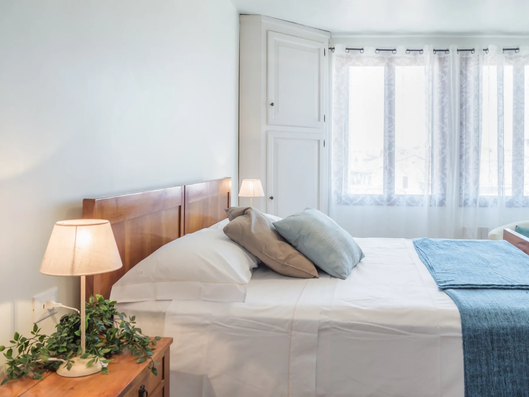 A bright bedroom with a neatly made bed and curtains over the window.