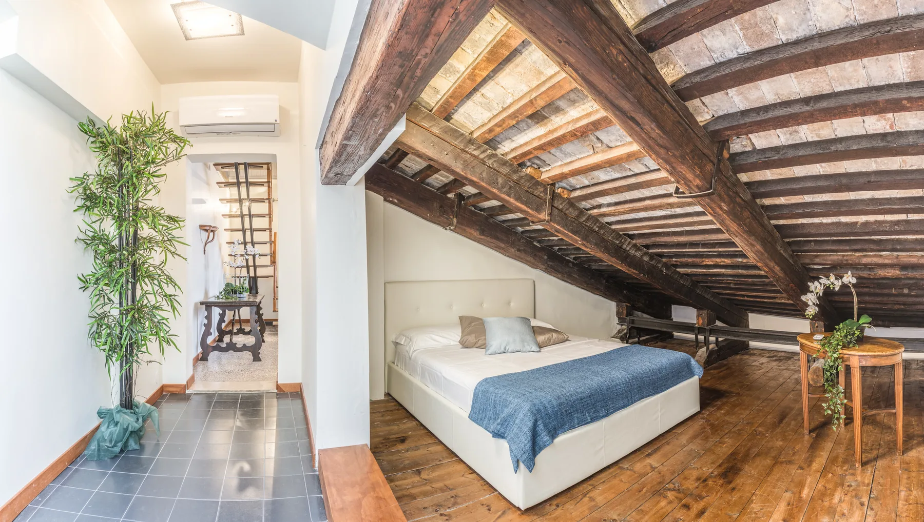 A bedroom with a bed beneath exposed wooden roof beams.