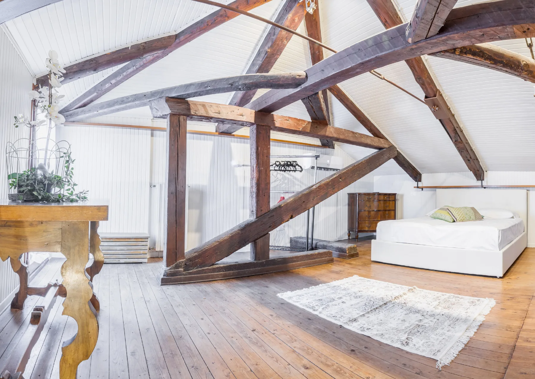A spacious loft bedroom with a white bed beneath exposed wooden roof beams.