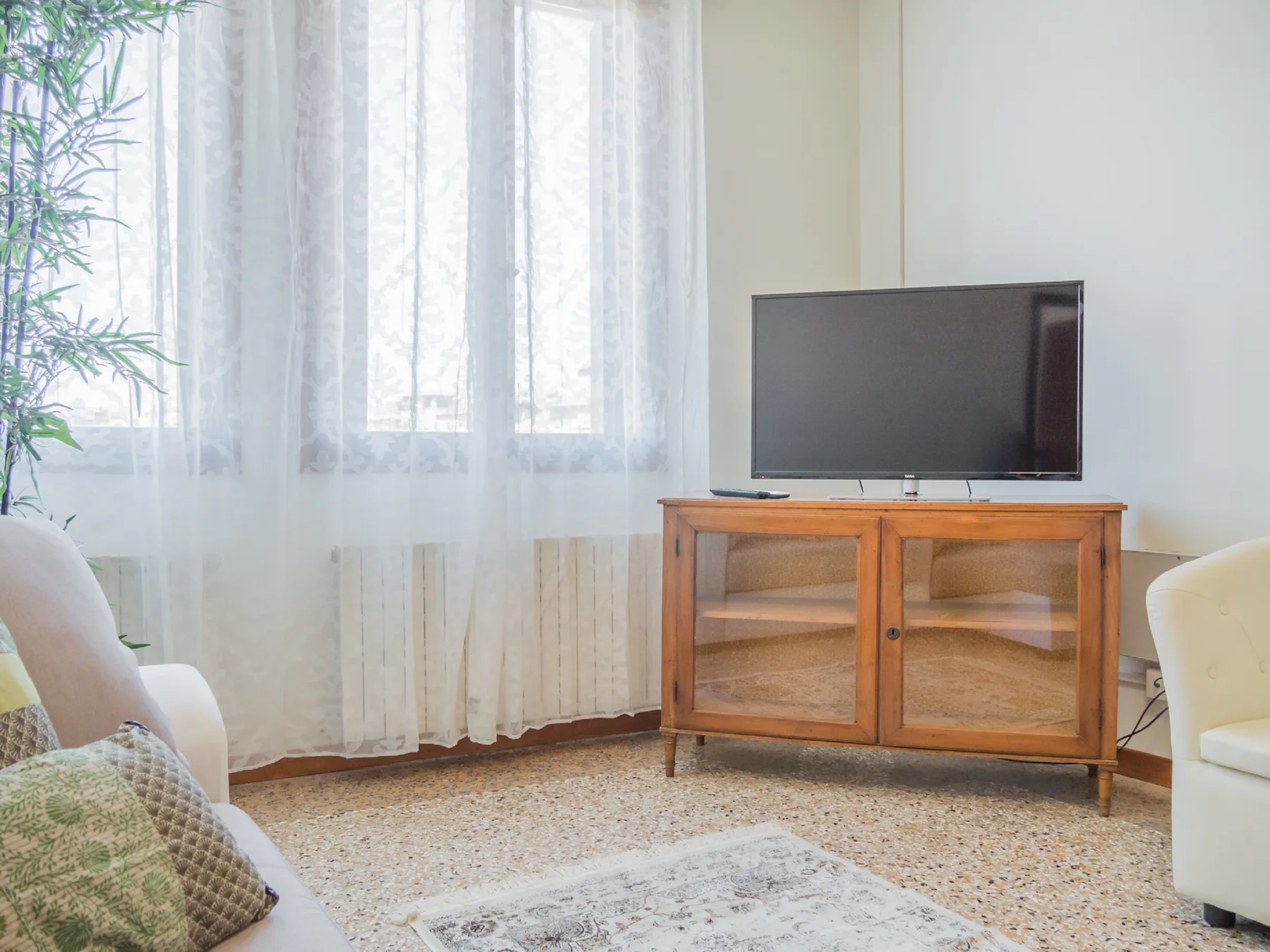 A living room with a television on a wooden cabinet beside curtained windows.