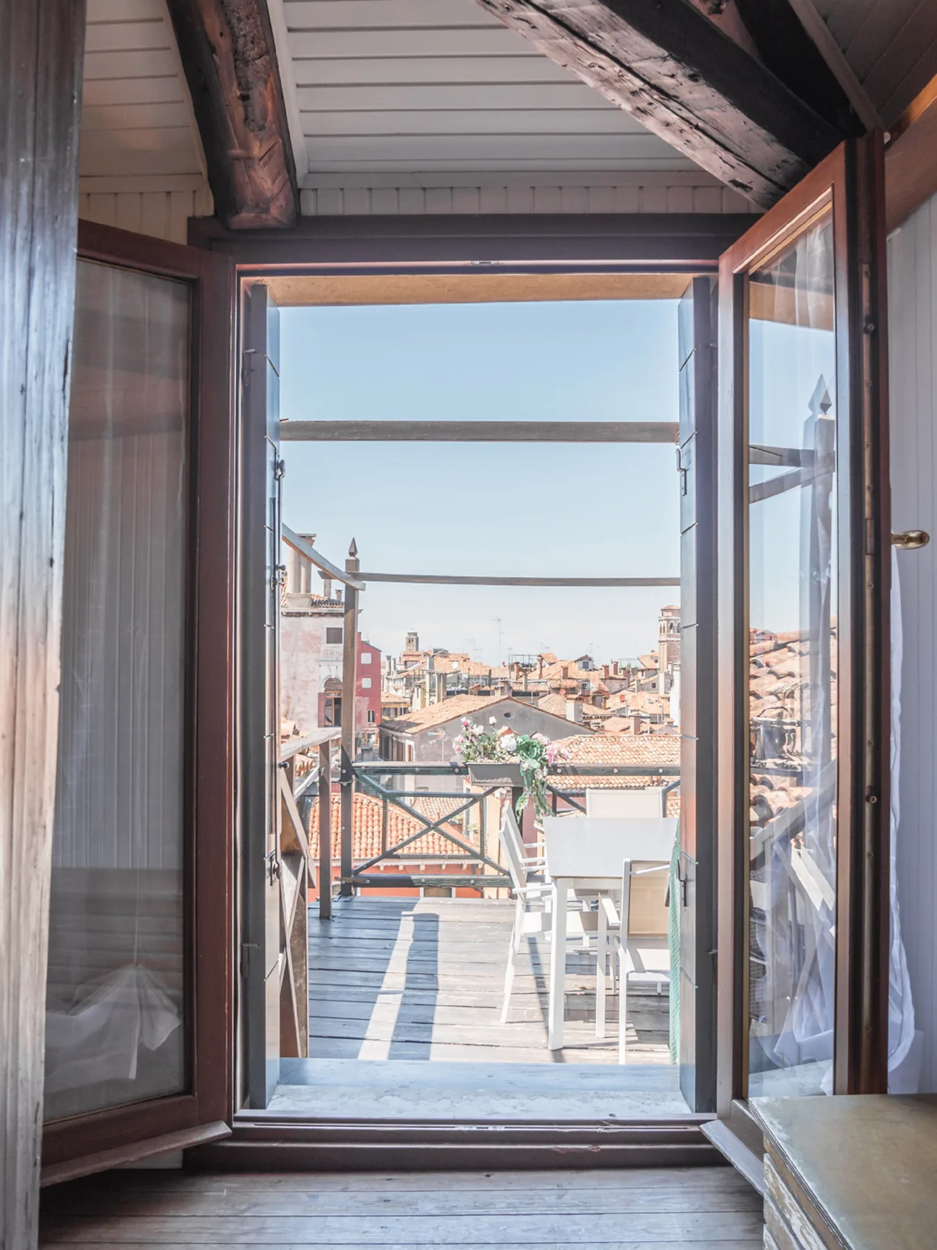 An open doorway leads to a balcony with seating and a view of nearby rooftops.