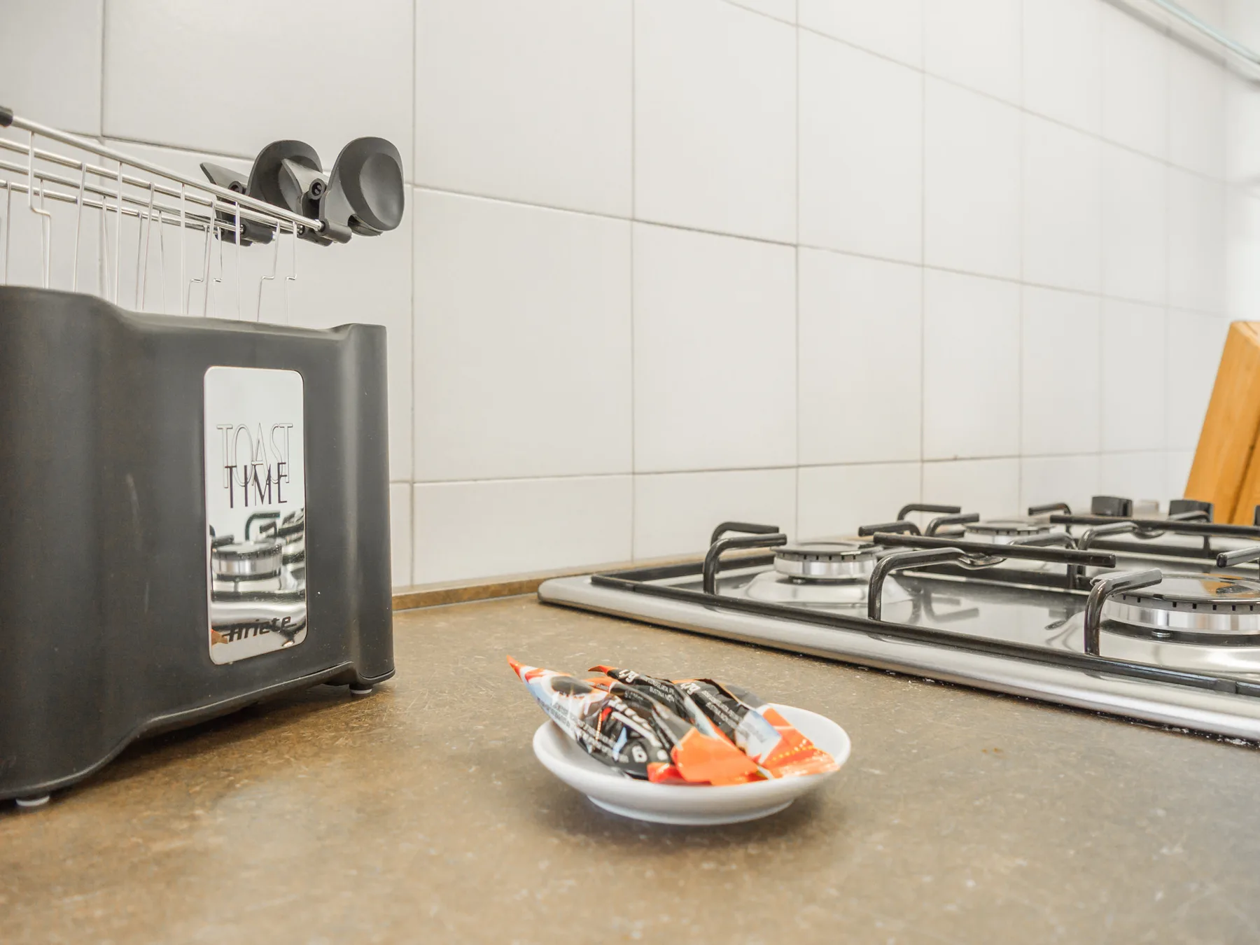 A tiled kitchen counter holds a gas cooktop and a small dish of packets.
