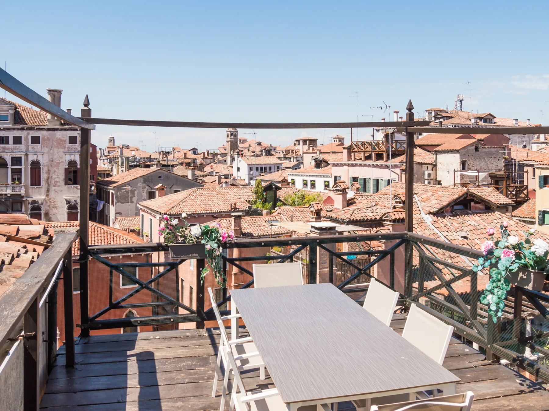 A rooftop terrace with a dining table overlooks a dense cityscape of tiled roofs.