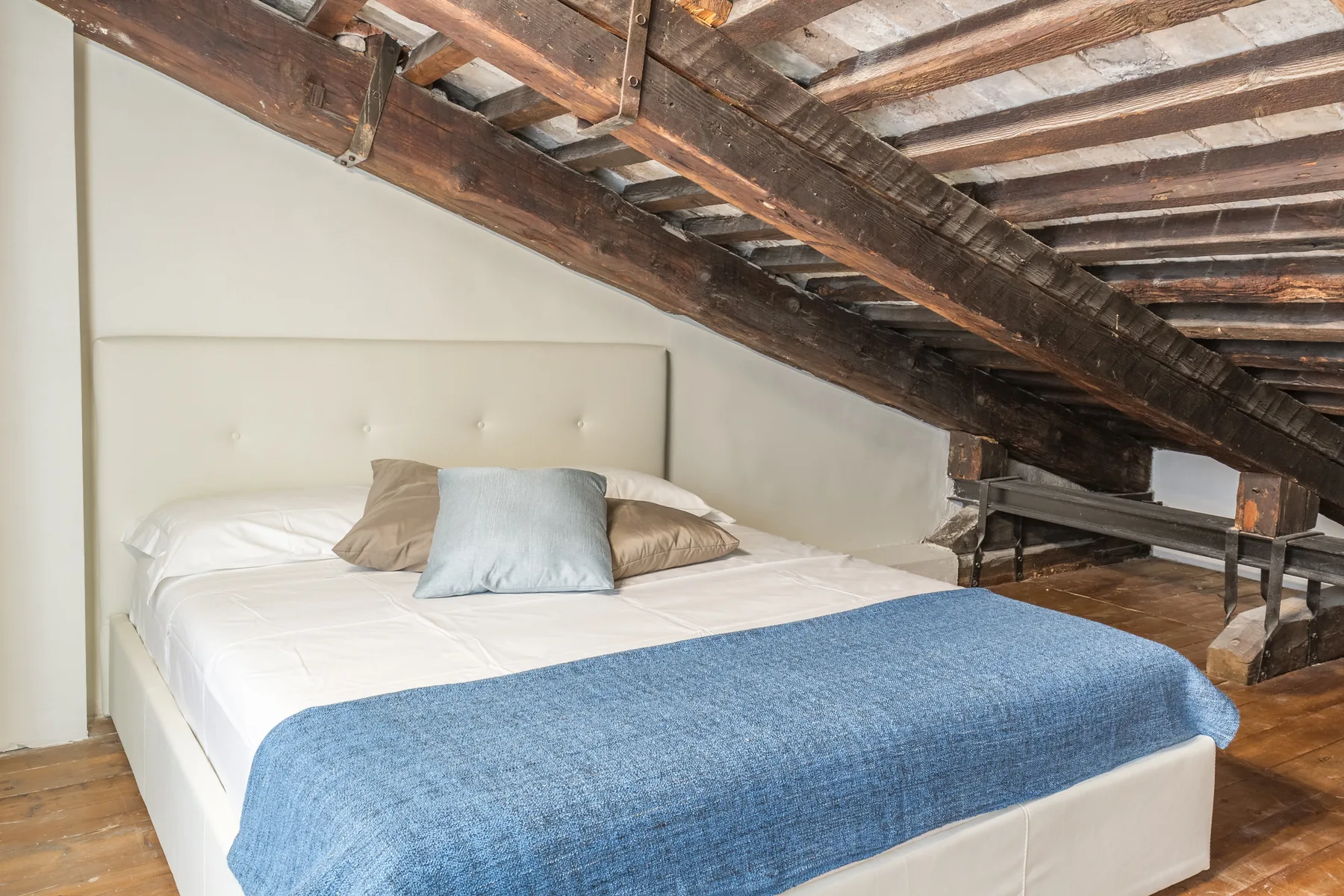 A bedroom with a bed beneath exposed wooden ceiling beams.