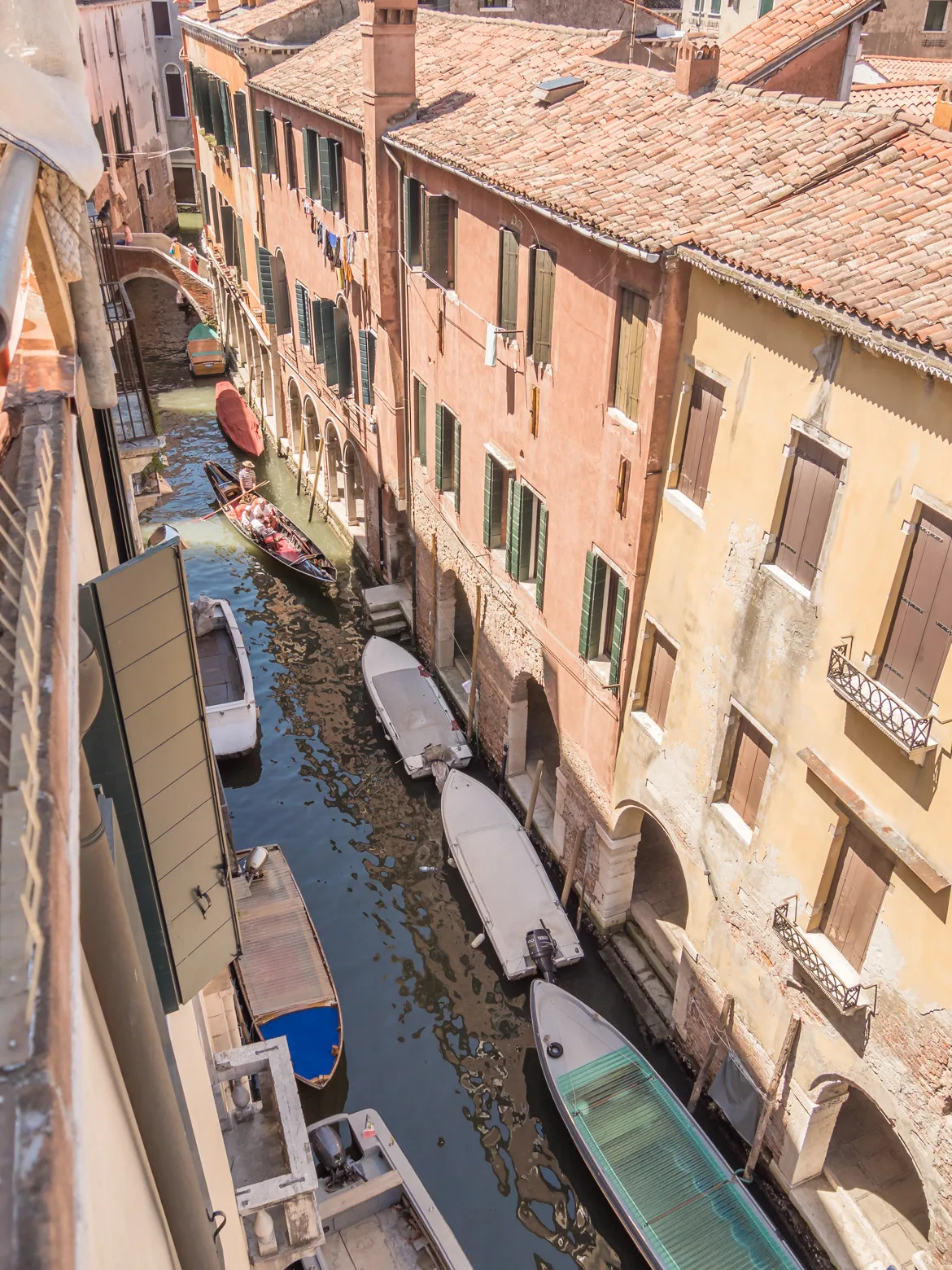 A narrow canal runs between closely spaced buildings, with boats along the water.