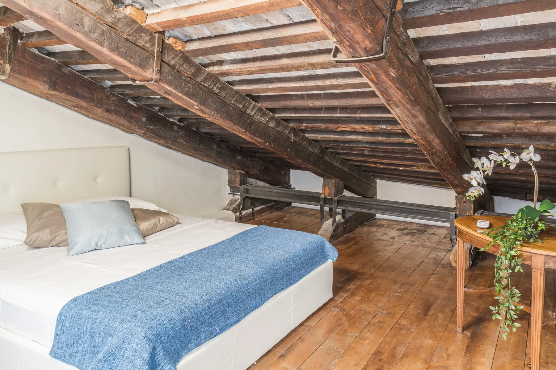 A bedroom with a bed beneath exposed wooden ceiling beams.