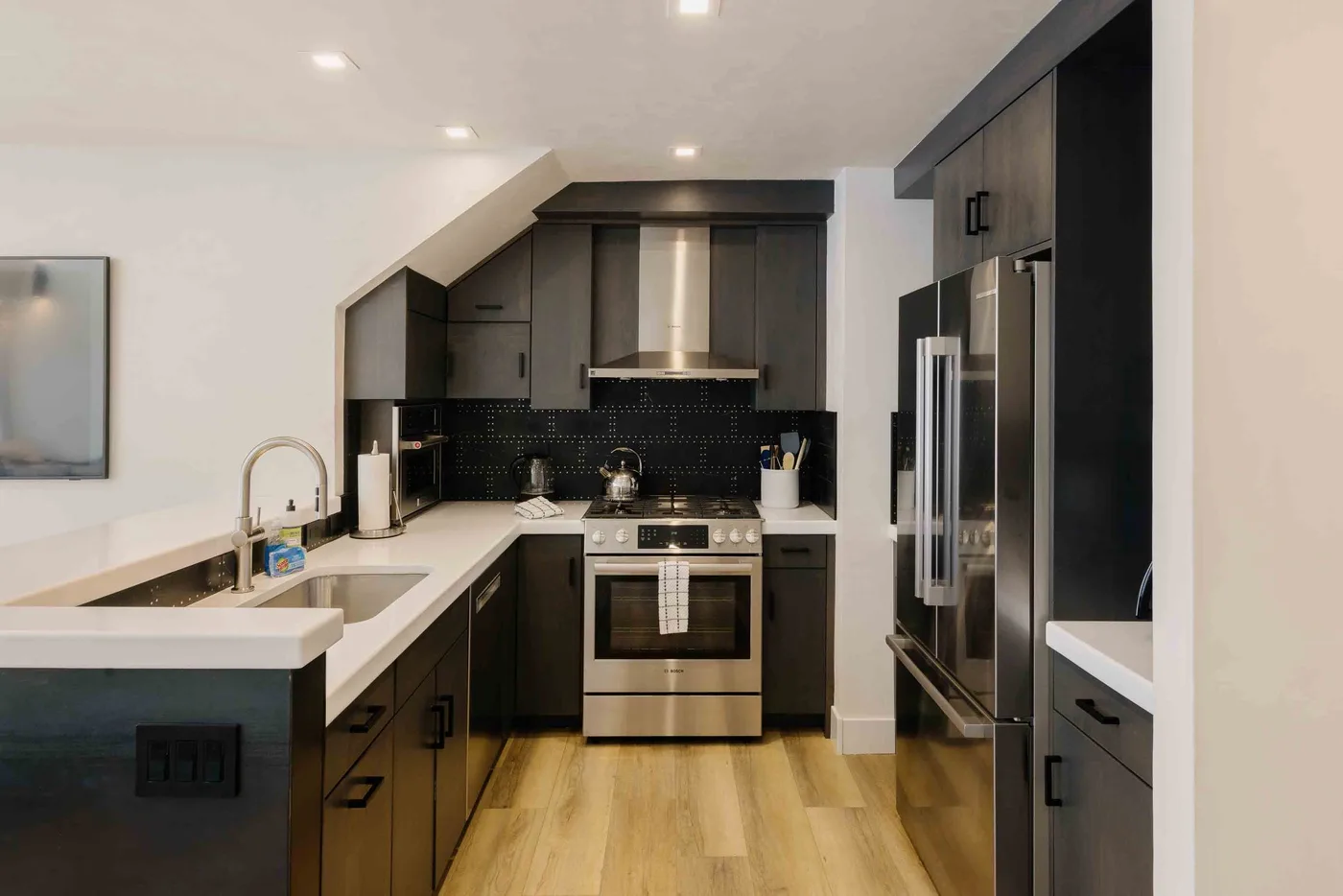 Una cocina moderna con gabinetes oscuros, electrodomésticos de acero inoxidable y piso de madera.