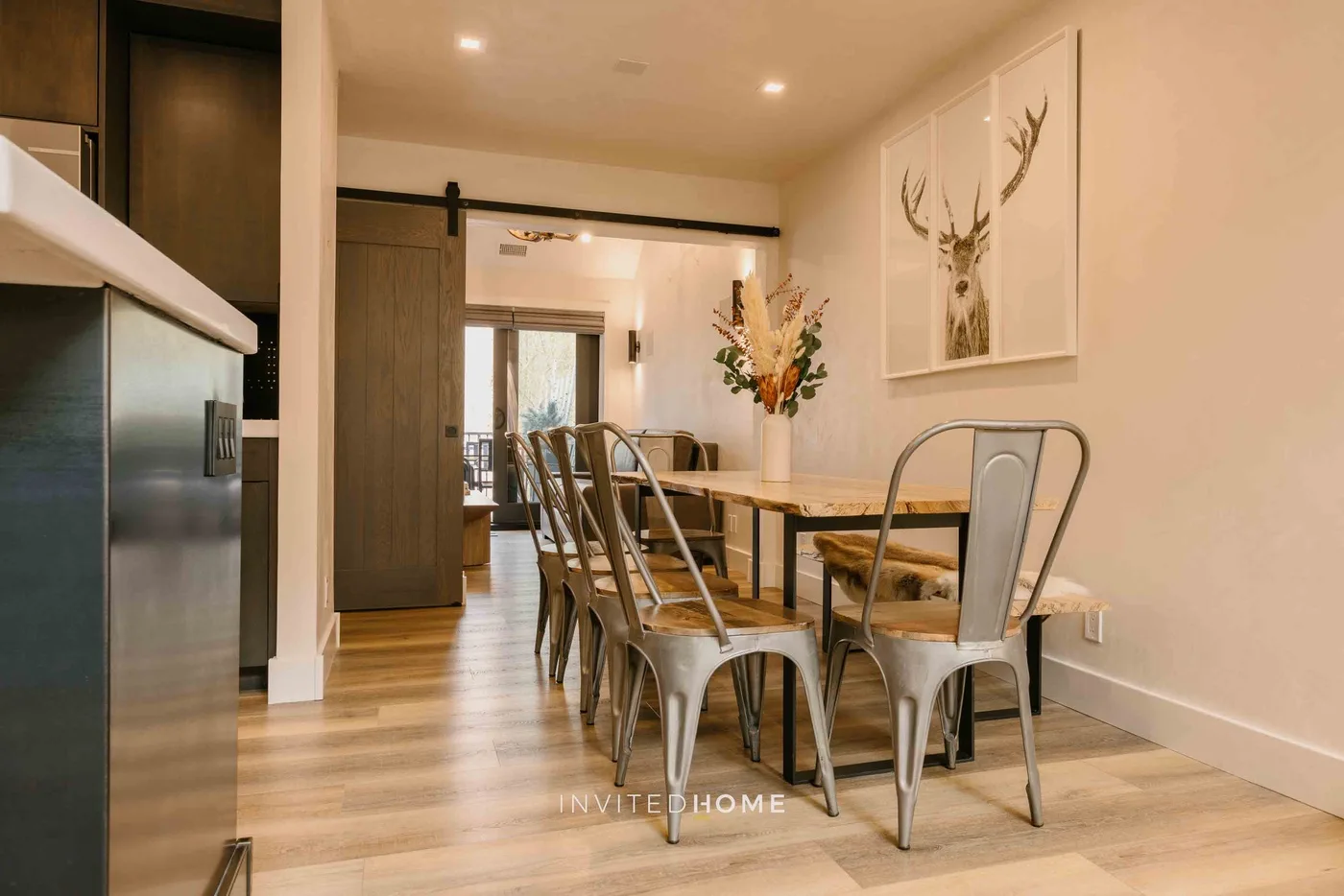 Comedor con mesa de madera, asientos metálicos y cuadros en la pared.