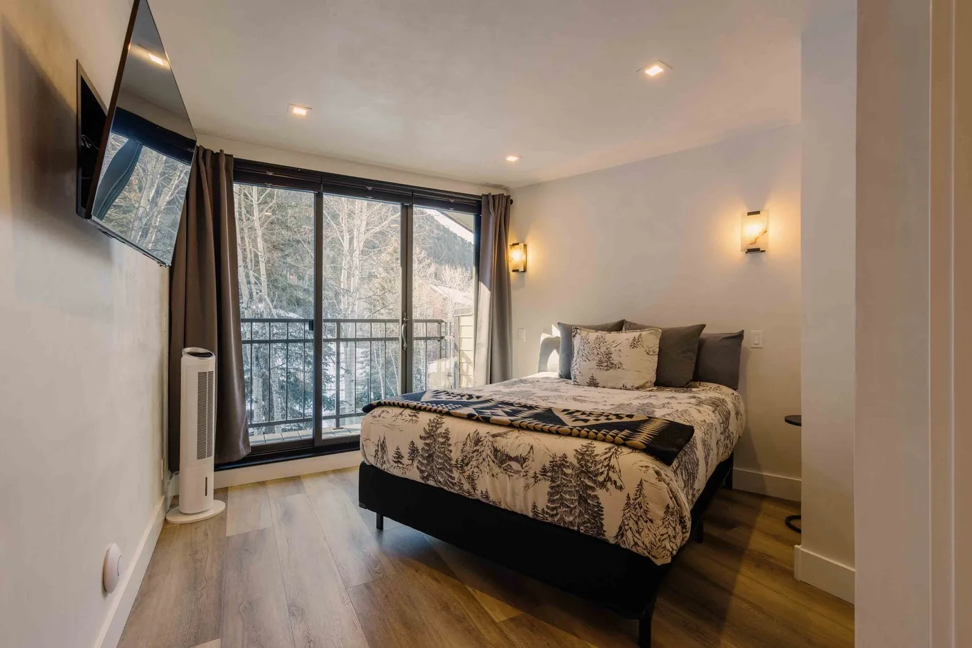 Un dormitorio con una cama junto a grandes ventanas con vistas a los árboles.