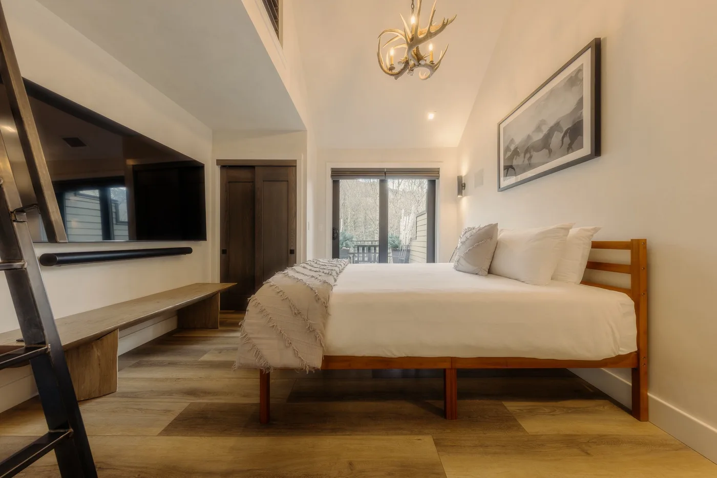 Un dormitorio con una cama bien tendida, un televisor montado en la pared y una obra enmarcada.