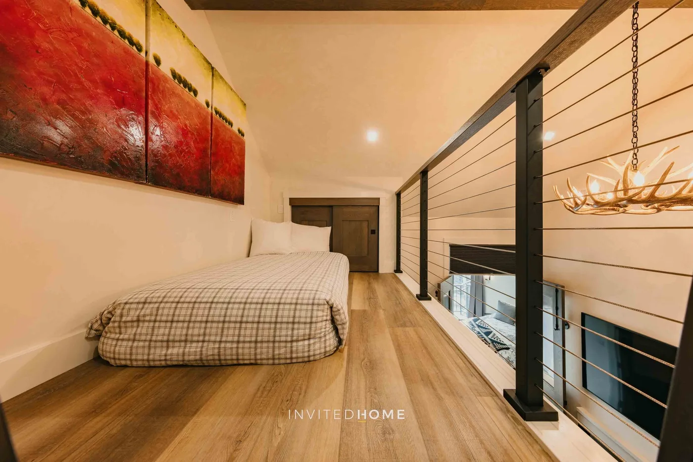 Un dormitorio tipo loft con una cama junto a una barandilla negra que da al piso inferior.