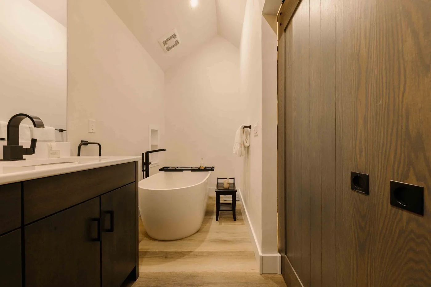Un baño con bañera exenta, lavabo con mueble y puerta de paneles de madera.