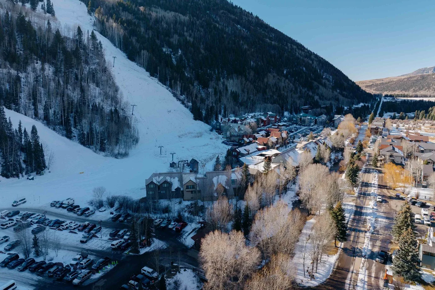 Un pueblo de montaña nevado se encuentra junto a una pista de esquí y colinas boscosas.