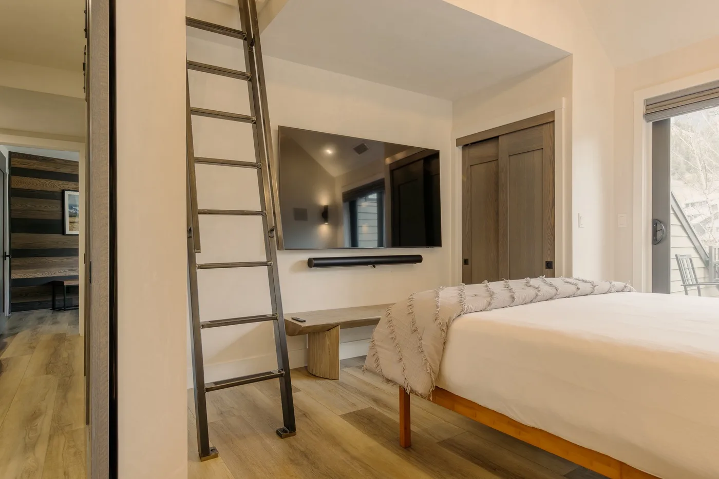 Un dormitorio con una cama, un televisor montado en la pared y una escalera junto a la pared.