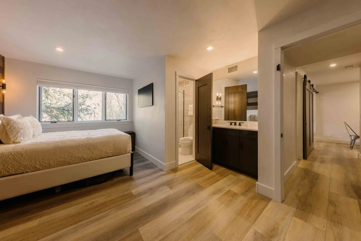 Un dormitorio con una cama junto a un lavabo de baño abierto y una ducha de vidrio.