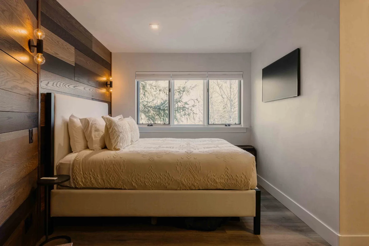 Un dormitorio con una cama bajo una ventana amplia y un televisor en la pared.