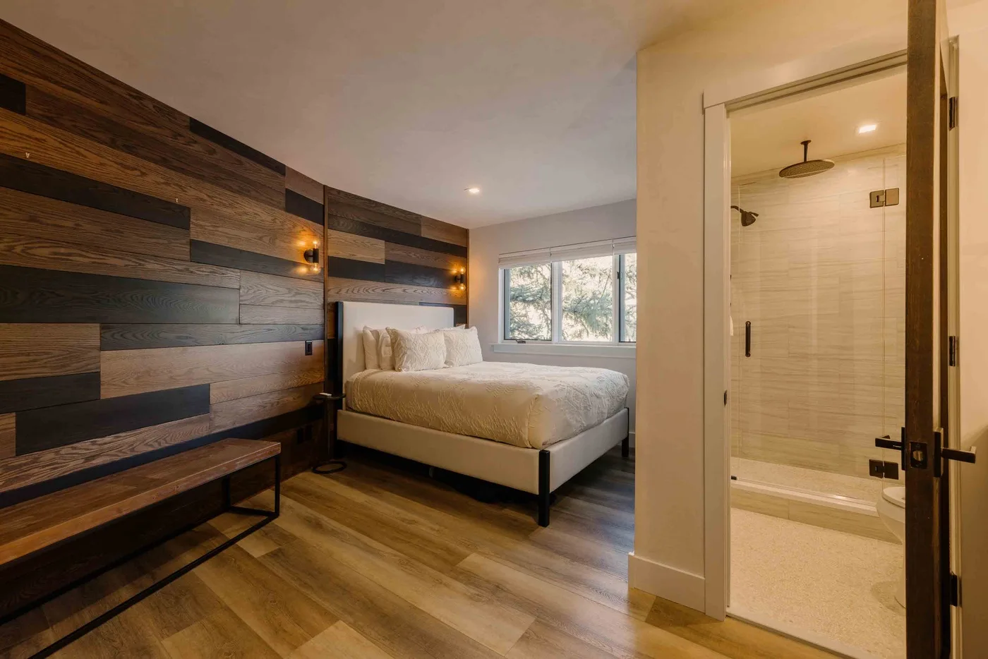 Un dormitorio con una cama junto a una pared revestida de madera y un baño abierto.
