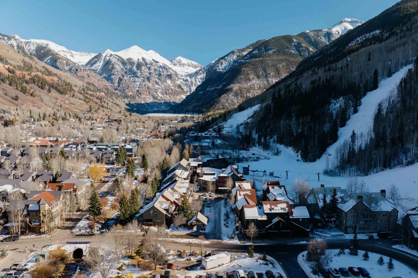Un pueblo de montaña se encuentra bajo picos nevados y una pista de esquí.