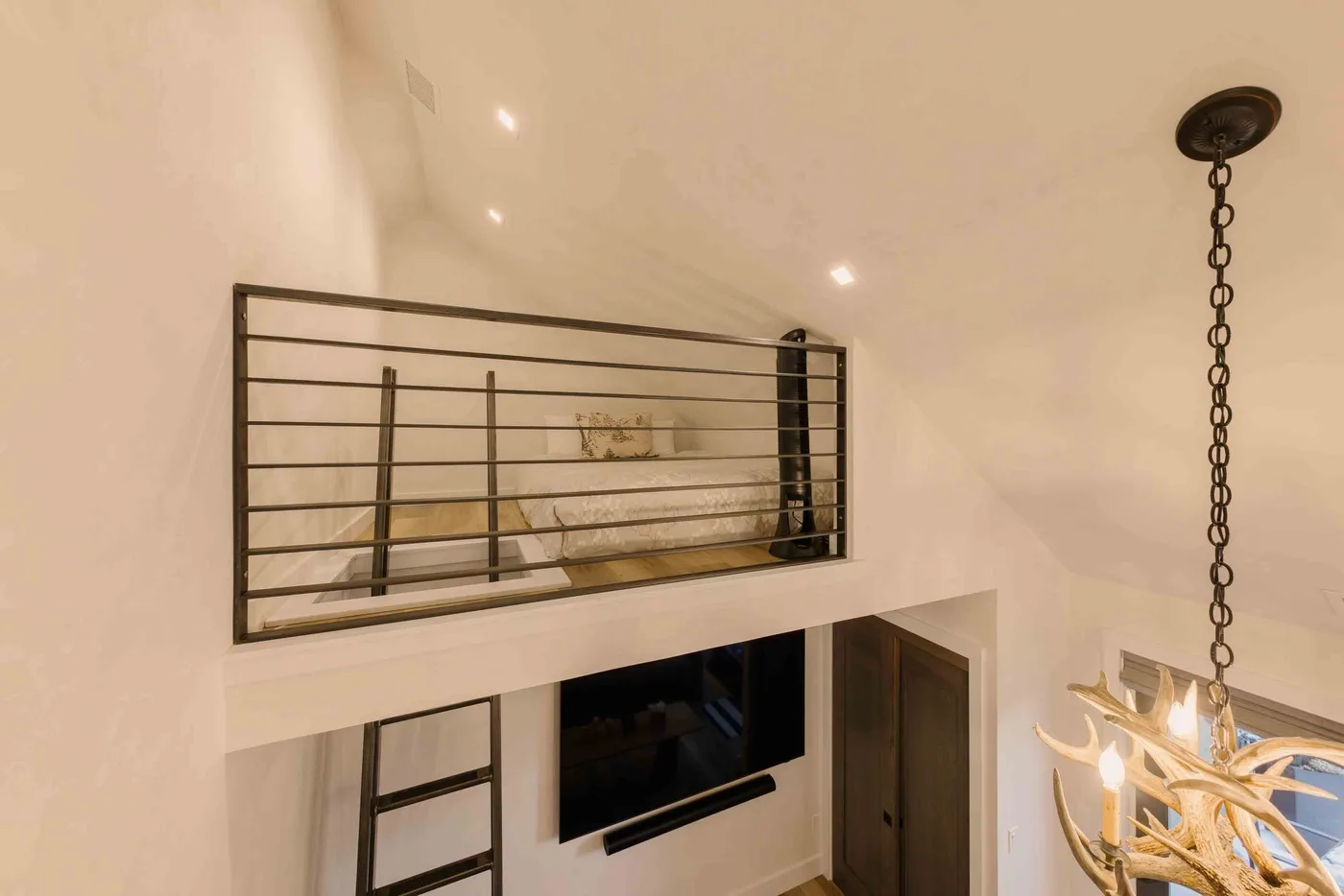 Un dormitorio tipo altillo da a una sala con televisor y lámpara colgante.