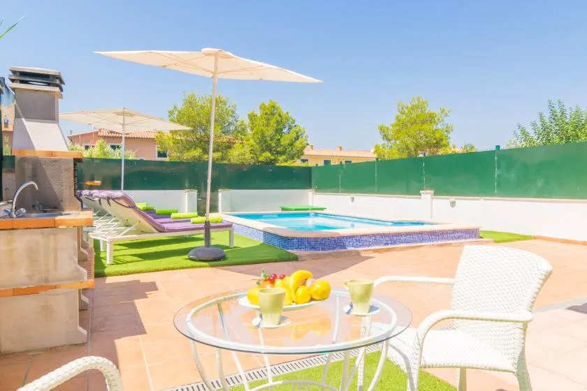An outdoor patio has a glass table, white seating, and a swimming pool.