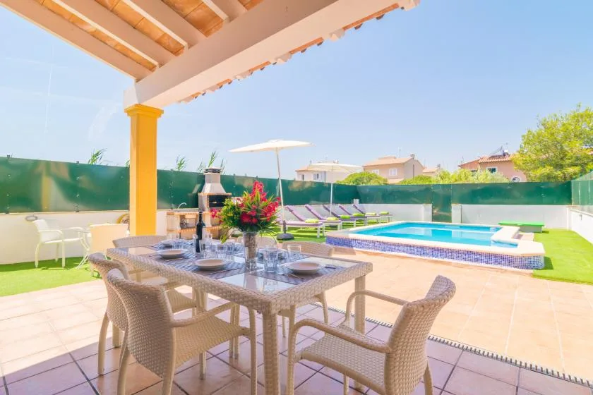 A covered outdoor dining area overlooks a swimming pool and green lawn.