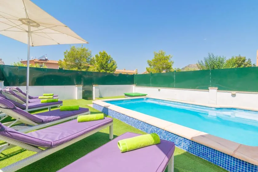 An outdoor swimming pool beside purple sun loungers and a large umbrella.