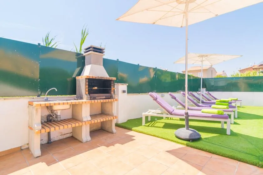 An outdoor patio has a built-in barbecue beside lounge chairs and umbrellas.