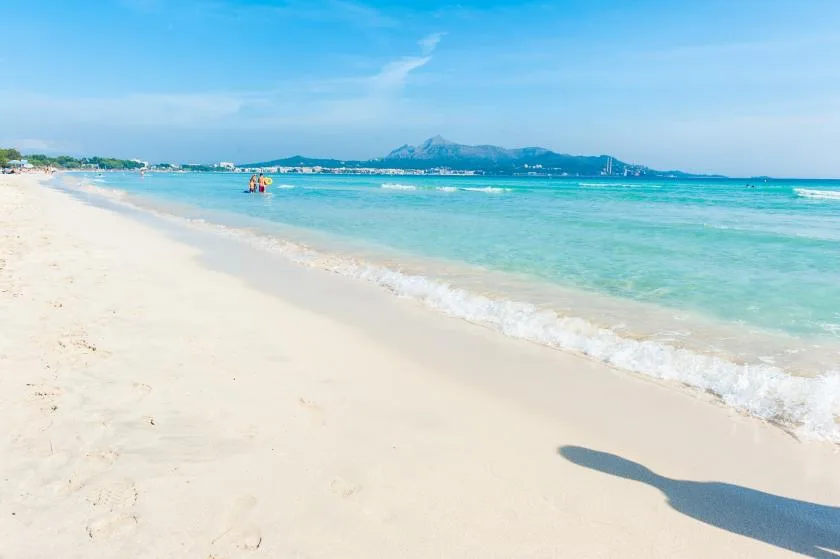 A sandy beach meets clear turquoise water beneath a blue sky.