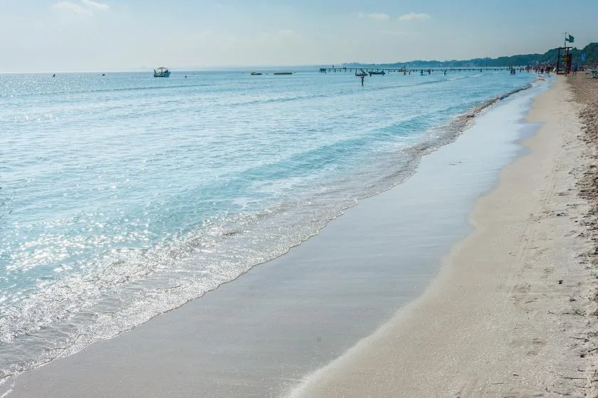 A sandy beach meets calm blue water beneath a clear sky.