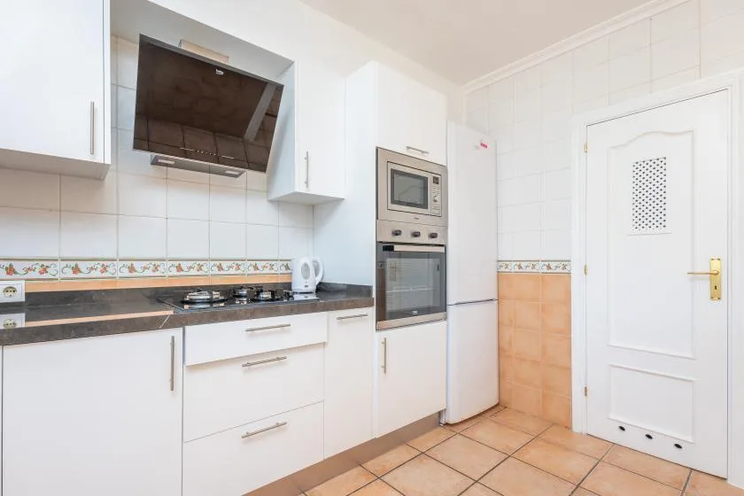 A tiled kitchen with white cabinets, a cooktop, and built-in appliances.