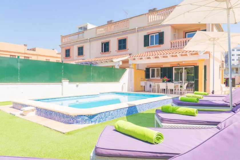 An outdoor pool sits beside purple lounge seating and a covered patio.