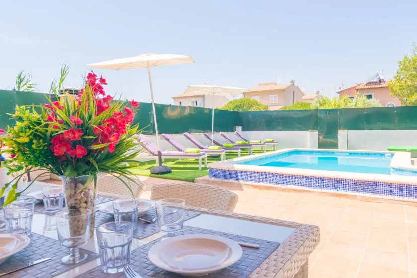 A sunny poolside patio with loungers, umbrellas, and an outdoor dining table.