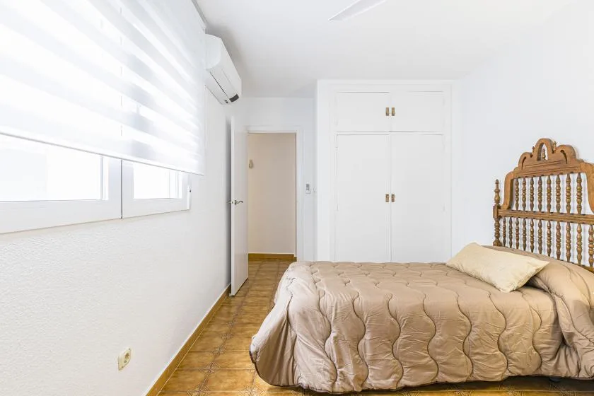 A bright bedroom with a bed, a built-in wardrobe, and a window with blinds.