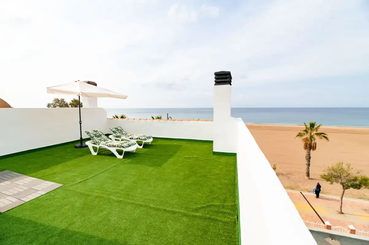 A rooftop terrace with green lawn overlooks the beach and sea.
