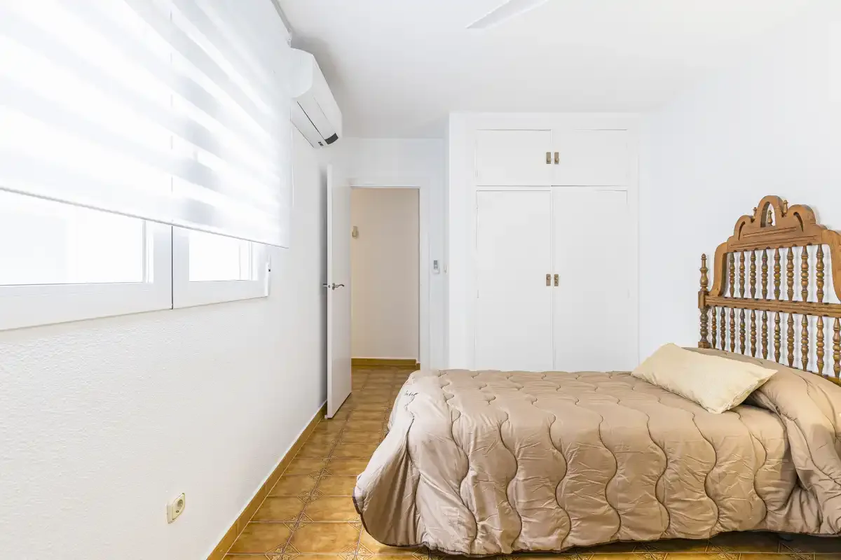 A bedroom with a bed, built-in storage, and a wide window.