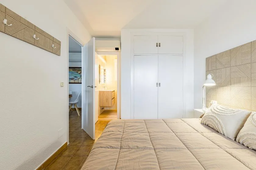 A bright bedroom with a large bed and built-in white wardrobes.