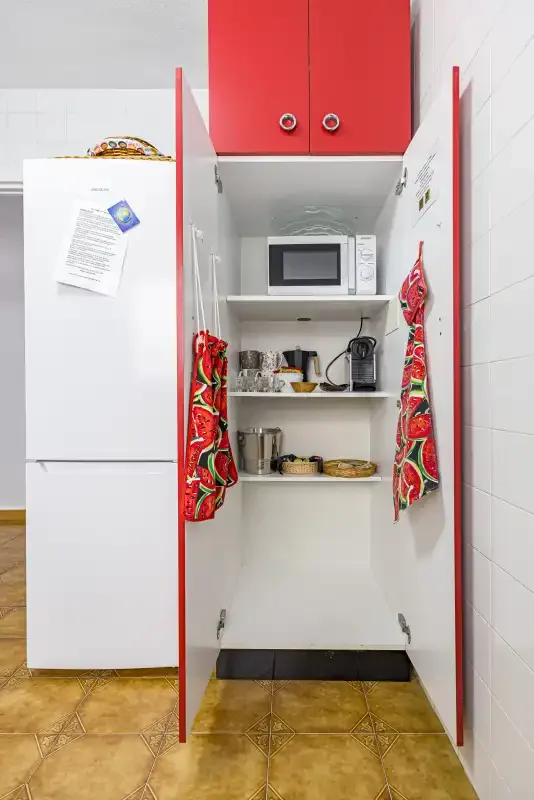 A kitchen storage cabinet stands open beside a refrigerator, with a microwave inside.