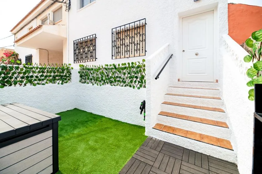 A small outdoor patio has green lawn, tiled steps, and a white entrance.