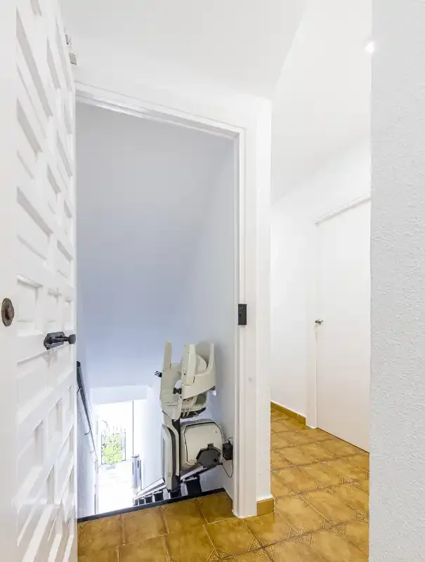 A bright interior hallway opens onto a stairwell beside a stairlift.