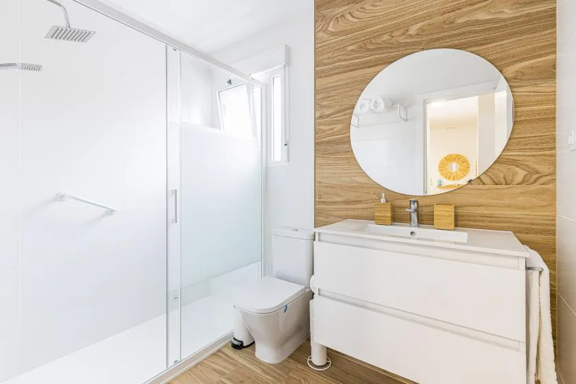 A bright bathroom with a glass shower, toilet, and vanity.