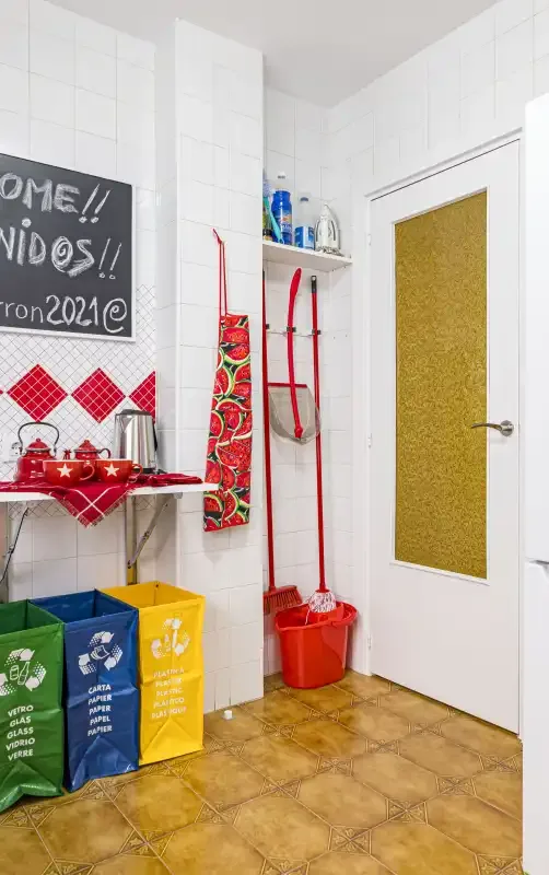 A tiled utility room with colorful recycling bags and cleaning tools.