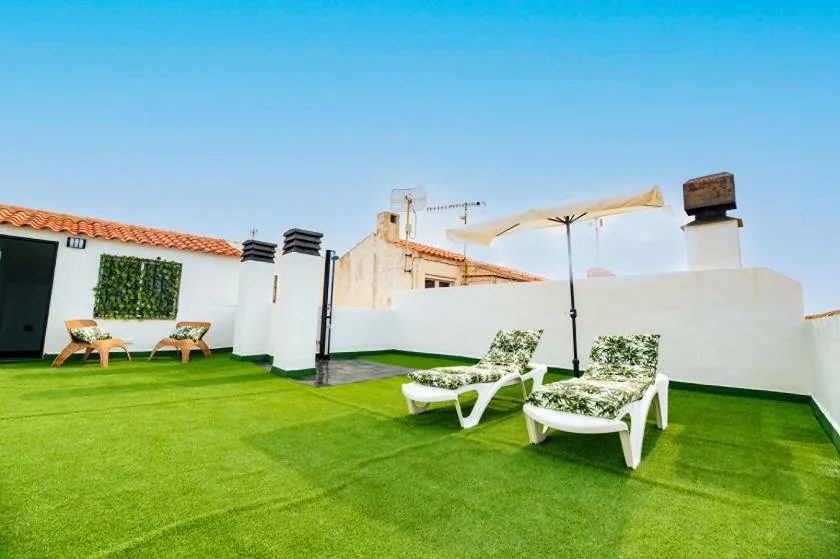 A rooftop terrace with green lawn, white loungers, and a shade umbrella.
